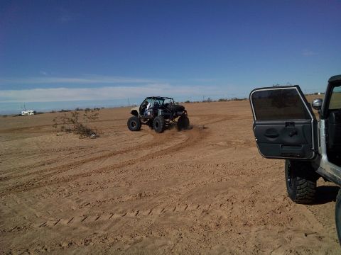2004 Jeep Wrangler - Two off-road vehicles are in a sandy desert landscape under a blue sky. The vehicle in the foreground is a silver Jeep Wrangler with its dr…
