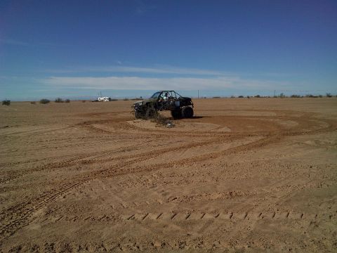 2004 Jeep Wrangler - A black off-road buggy is shown kicking up dust in a sandy desert landscape, leaving tire tracks in a circular pattern. In the background,…