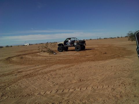 2004 Jeep Wrangler - A custom off-road buggy with a roll cage and large tires is shown in a sandy desert landscape. The vehicle is turning, leaving tire tracks…