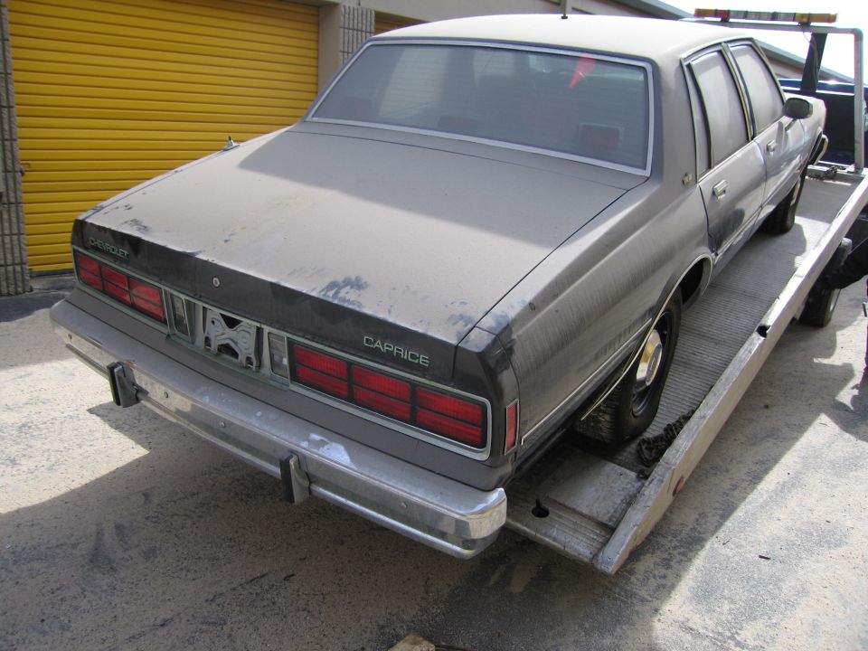 Rear view of a dusty Chevrolet Caprice being loaded onto a tow truck