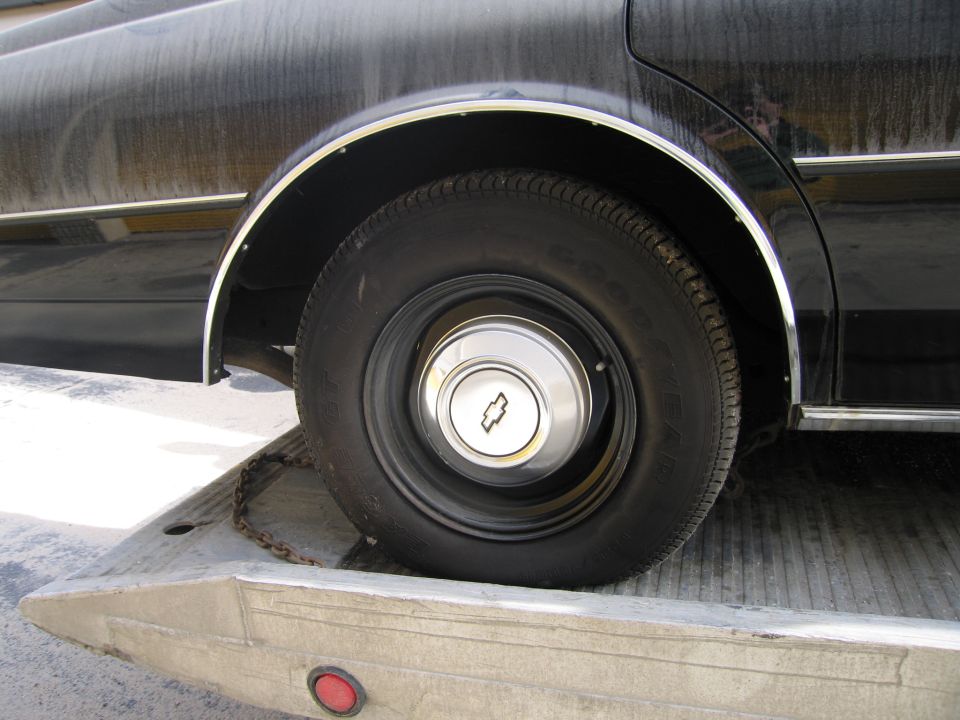 Front wheel of a black Chevrolet sedan with bowtie hubcap on a flatbed