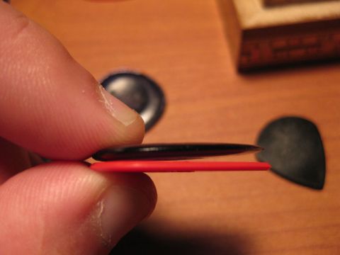 1989 Mazda MX-6 - A hand holds two guitar picks, a black one over a red one, with other picks blurred in the background.