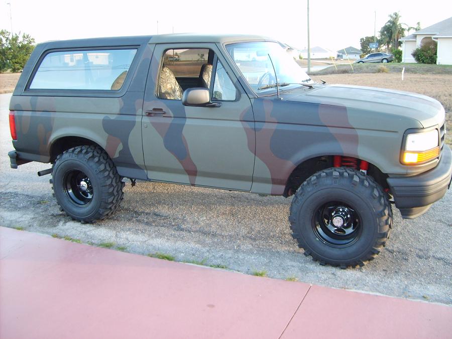 Camouflaged Ford Bronco with lifted suspension and off-road tires, viewed from the front three-quarter angle