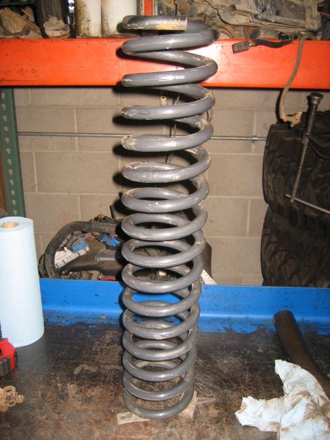 1990 Ford Bronco - A single gray coil spring is shown on a workbench, possibly for a vehicle suspension system.