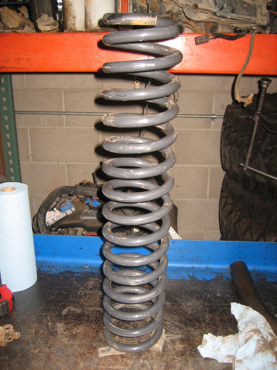 Gray coil spring on a workbench with tools and a roll of paper towels