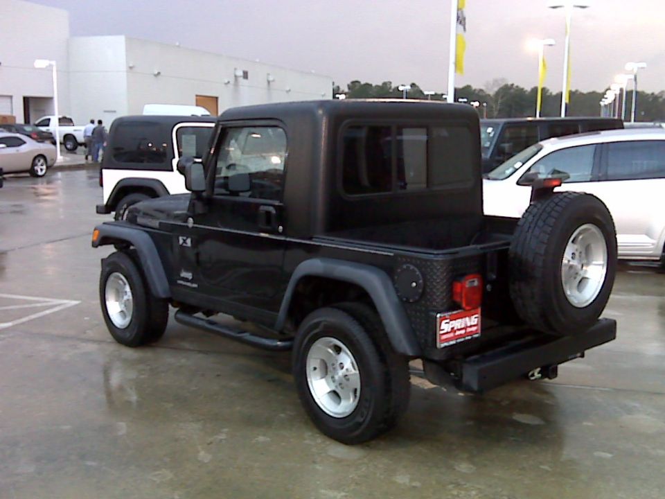 Black Jeep Wrangler with a custom pickup bed conversion, parked outside a building with other vehicles