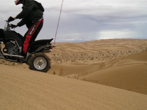 1986 Toyota Hilux - Riding a quad bike up a sand dune in a desert landscape. "SUPERMOTORS" logo is visible.