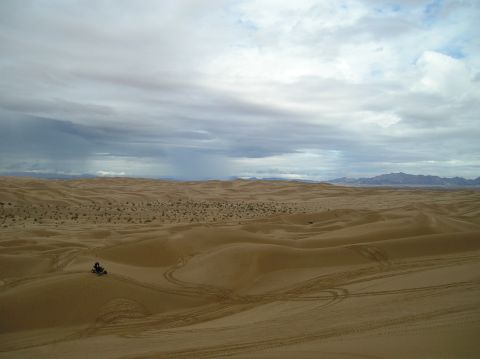 1986 Toyota Hilux - An ATV navigates the vast sand dunes, leaving tracks behind under a dramatic, cloudy sky.