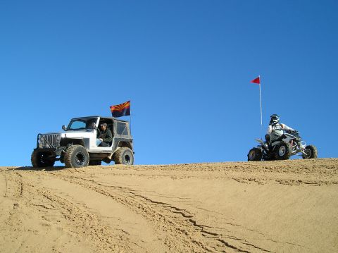 1986 Toyota Hilux - Two off-road vehicles, a Jeep and an ATV, traverse a sandy landscape on a clear day.