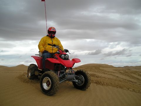 1986 Toyota Hilux - A rider on a red ATV navigates a sandy terrain under a cloudy sky.
