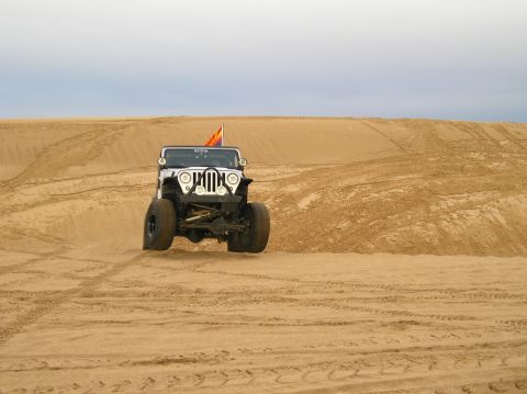 1986 Toyota Hilux - Jeep Wrangler navigating sandy terrain with tire tracks visible on the dunes.