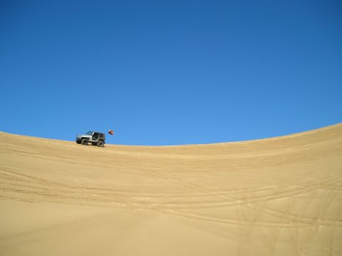 1986 Toyota Hilux - A white off-road vehicle navigates a sandy terrain under a vast blue sky.