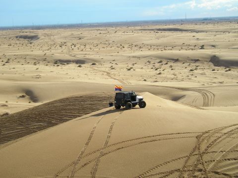 1986 Toyota Hilux - Off-road vehicle navigating sand dunes under a clear sky. Tire tracks mark the sandy terrain.
