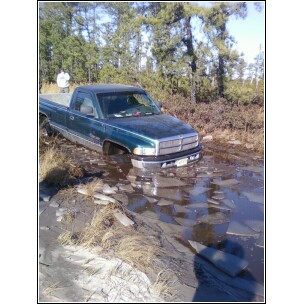 2004 Jeep Wrangler - A green pickup truck is stuck in a watery area with ice fragments scattered around.