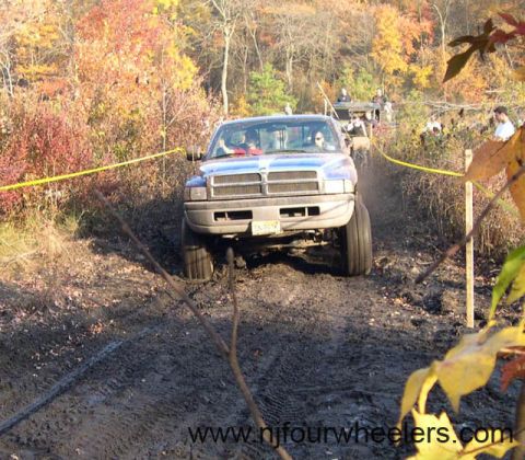 2004 Jeep Wrangler - A lifted Dodge Ram truck navigates a muddy off-road course with other vehicles present.