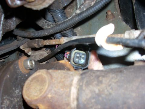 2000 Chevrolet Tahoe - Vehicle electrical connector near a rusty exhaust pipe, likely part of an engine or drivetrain.