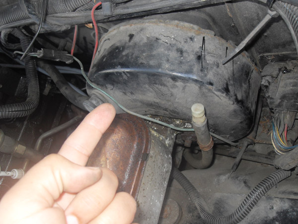Hand pointing at a rusty fuel tank and components under a vehicle