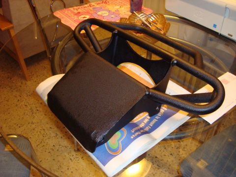 1995 Mazda MX-6 - A black metal part, possibly a vehicle accessory, rests on a newspaper the SuperMotors logo.