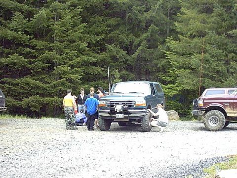 1995 Ford Bronco - Group of people gathered around a 1995 Ford Bronco and a Ford F-Series truck in a wooded area.