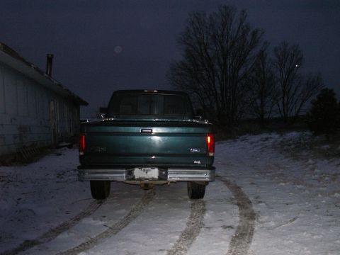 1997 Ford F-250 - A green 1997 Ford F-250 pickup truck is parked in a snowy area at dusk, with tire tracks visible.