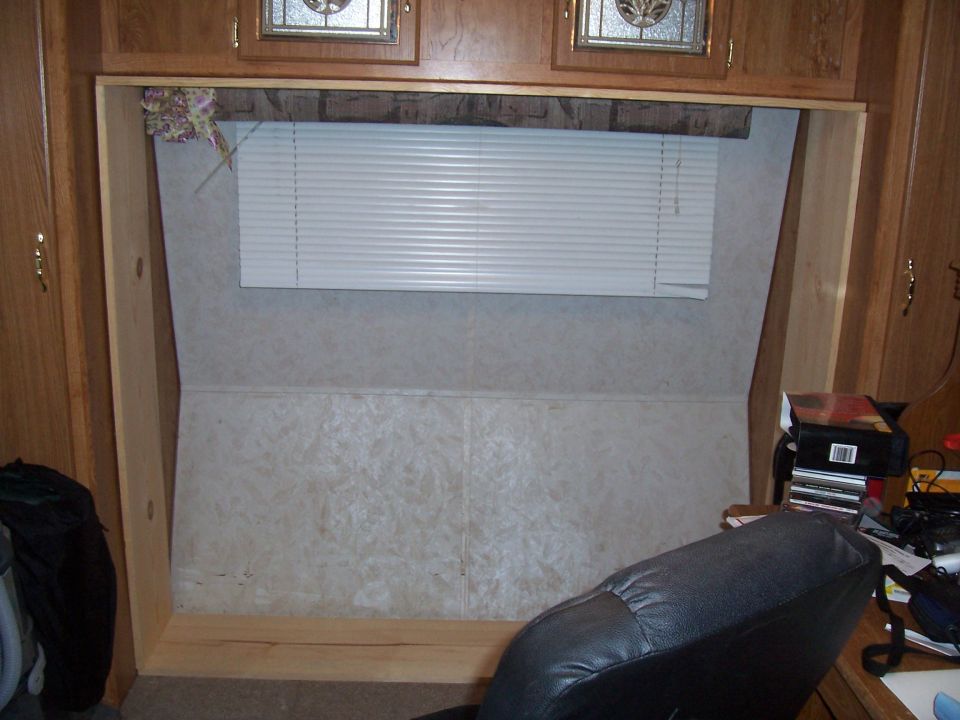 Interior view of a room with wooden cabinets above a window with white blinds. A black chair is in the foreground