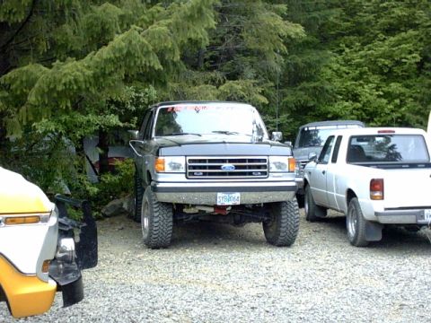 1995 Ford Bronco - A lifted Ford F-Series truck is parked outdoors with other vehicles and trees in the background.
