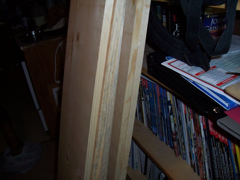 Stack of unfinished lumber in front of a bookshelf filled with magazines and books