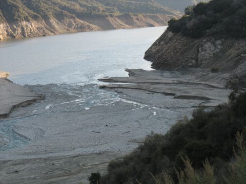 1987 Ford Bronco - A dry riverbed flows into a lake, bordered by steep, rocky hills and vegetation.