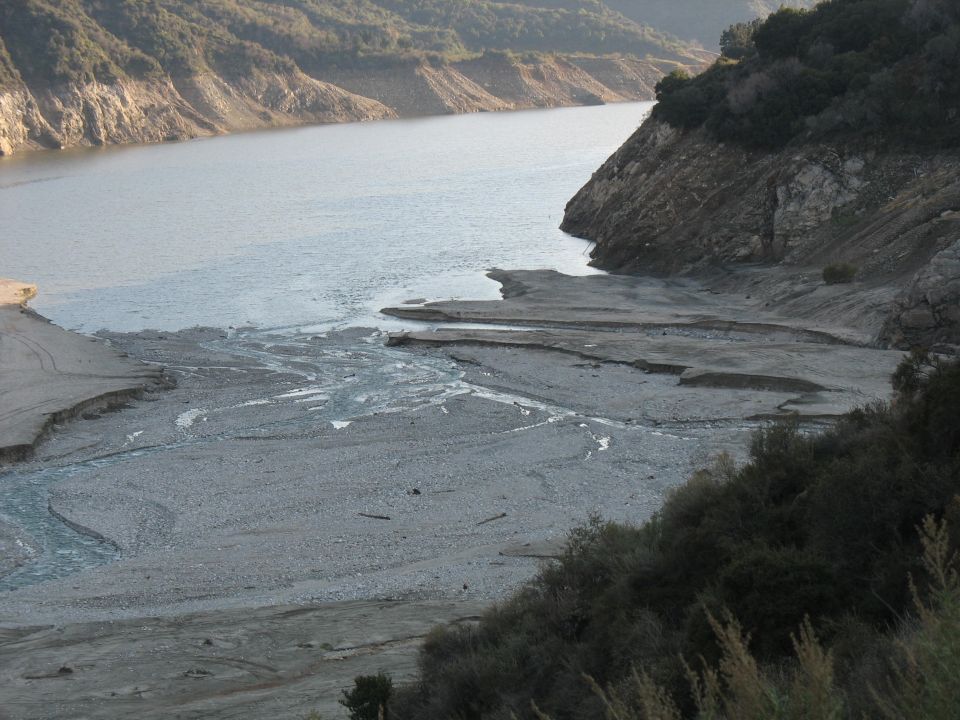 Dry riverbed leading to a lake with rocky hillsides