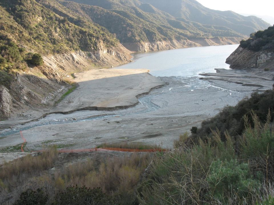 Dry lake bed with mountains and a body of water in the distance. Orange fencing is visible in the foreground