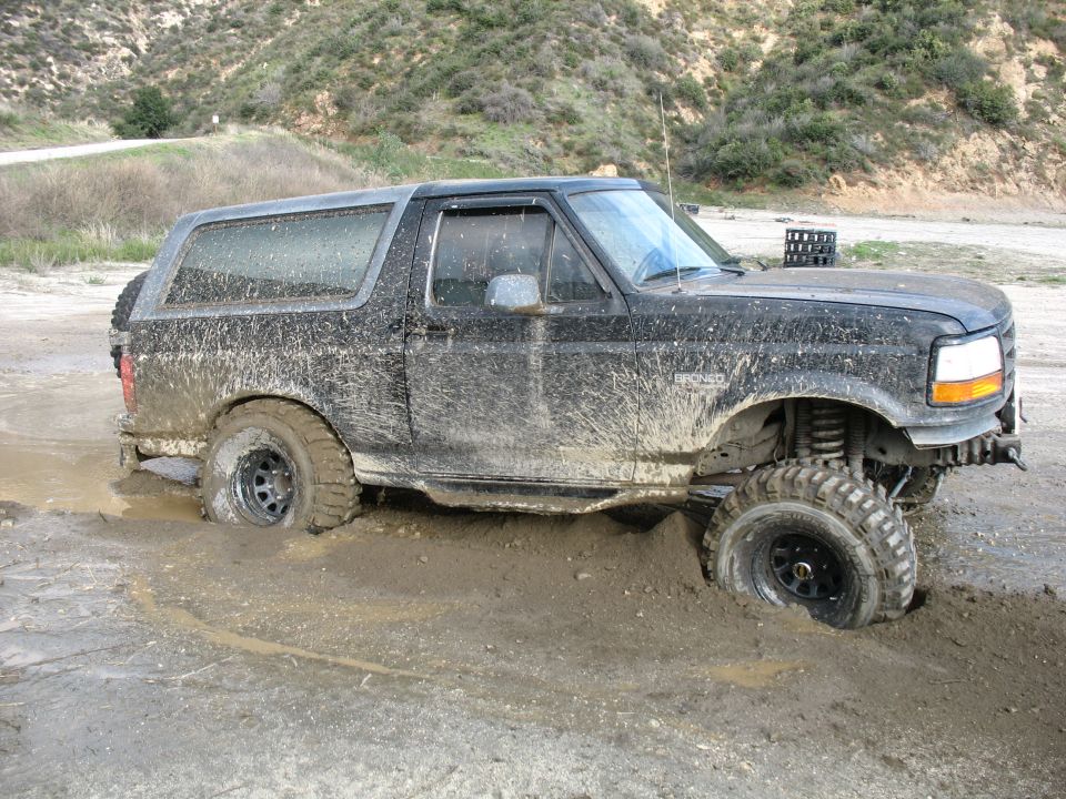 Muddy black SUV stuck in a mud pit, front right wheel submerged