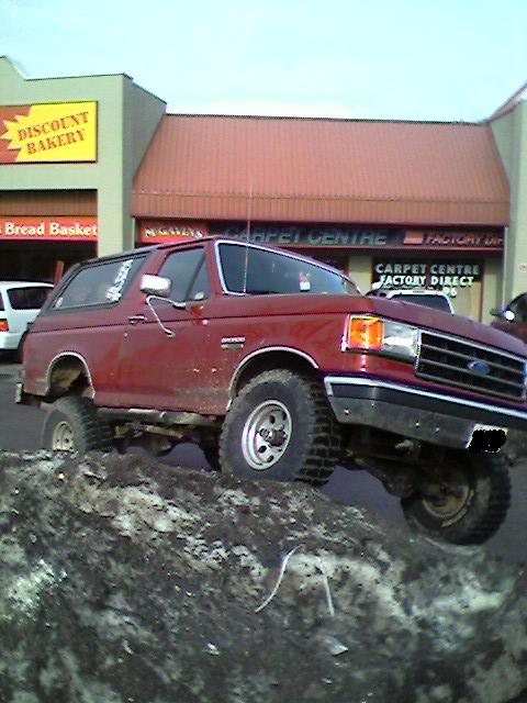 1989 Ford Bronco - A red 1989 Ford Bronco navigates a snow pile in front of a Discount Bakery and Carpet Centre.