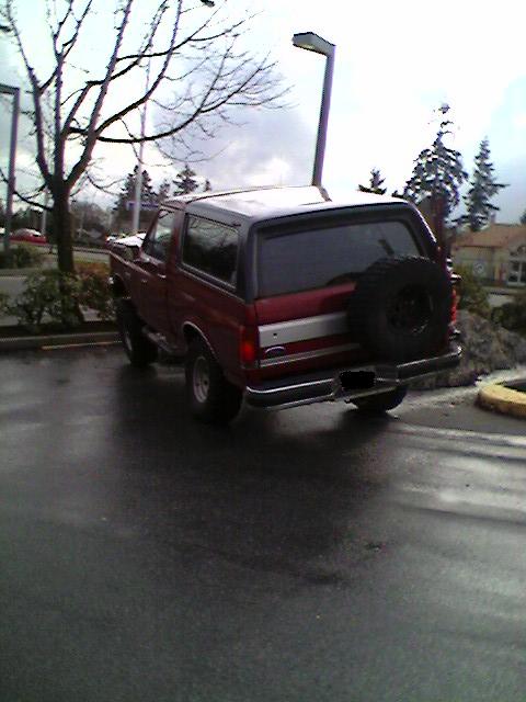 1989 Ford Bronco - This red Ford Bronco is parked outside on a cloudy day, showing its rear profile and spare tire.