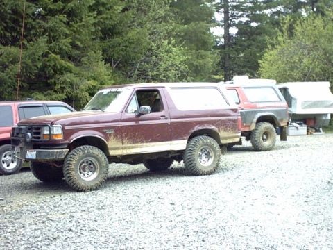 1995 Ford Bronco - A maroon Ford Bronco is parked on a gravel lot, with another Bronco and a trailer behind it.