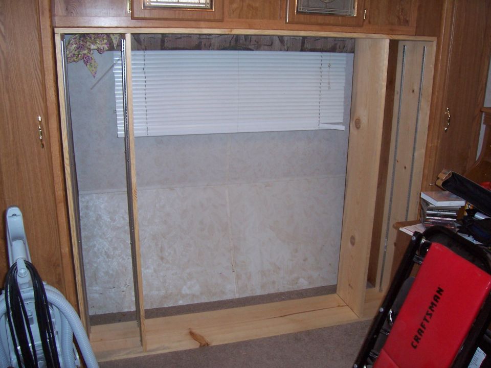 Unfinished wooden frame in a room with a window blind and patterned wallpaper