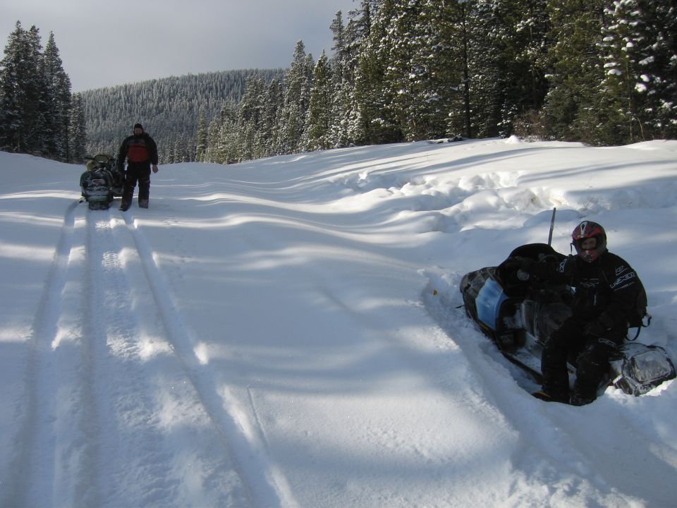 Two snowmobiles parked on a snow-covered trail with trees in the background