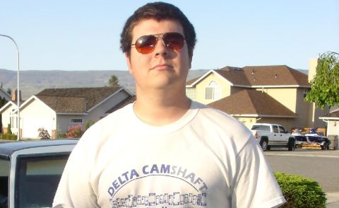 1978 Ford Mustang II - A man stands in front of houses and vehicles, wearing a t-shirt with text that reads 'Delta Camshaft'.