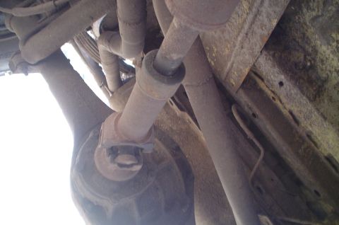 1979 Ford Bronco - The undercarriage of a vehicle shows rusty metal parts and exhaust pipes.