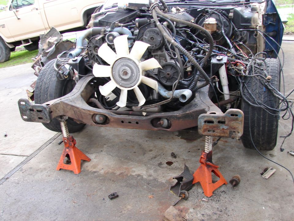 Stripped front end on jack stands showing V8, white clutch fan and loose wiring
