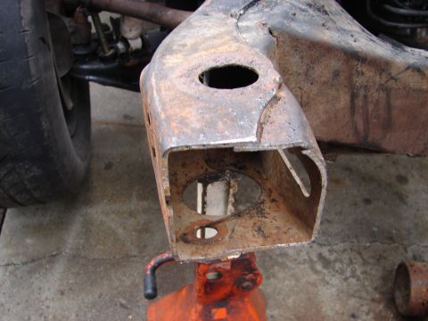 1973 Ford Ranchero - Rusted vehicle frame part is held up by an orange jack stand on a concrete surface.