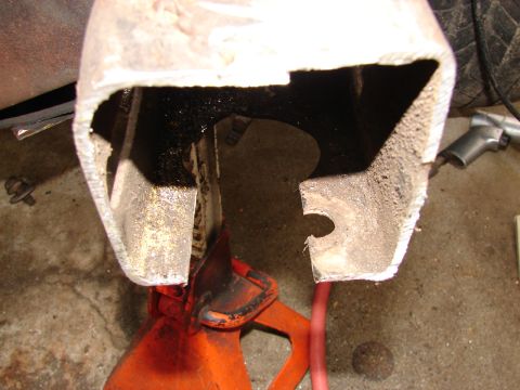 1973 Ford Ranchero - Close-up of a cut-open boxed frame or body-mount section revealing heavy rust and grime inside, supported on an orange jack stand on a gara…