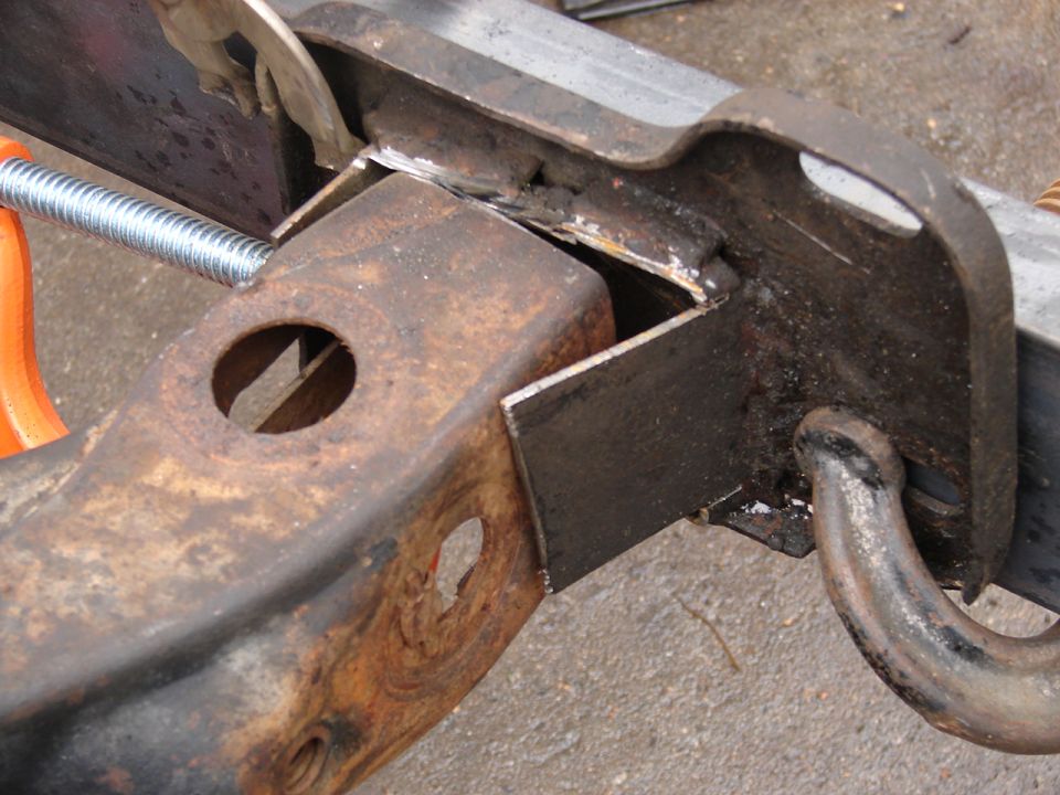 Rusty steel frame bracket tack-welded and clamped, with black tow hook bolted through