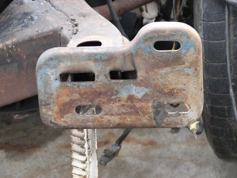 1973 Ford Ranchero - Close-up of a slotted steel bracket welded to a rear axle housing, viewed from behind with a tire and brake hardware in the background. The…