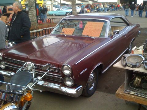 1983 Ford Bronco - A maroon coupe, possibly a 1965 model, is displayed with a motorcycle in front and various parts for sale nearby.