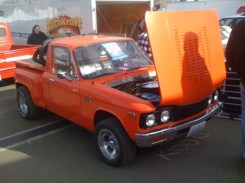 1983 Ford Bronco - An orange pickup truck is displayed with its hood open, parked next to another vehicle.