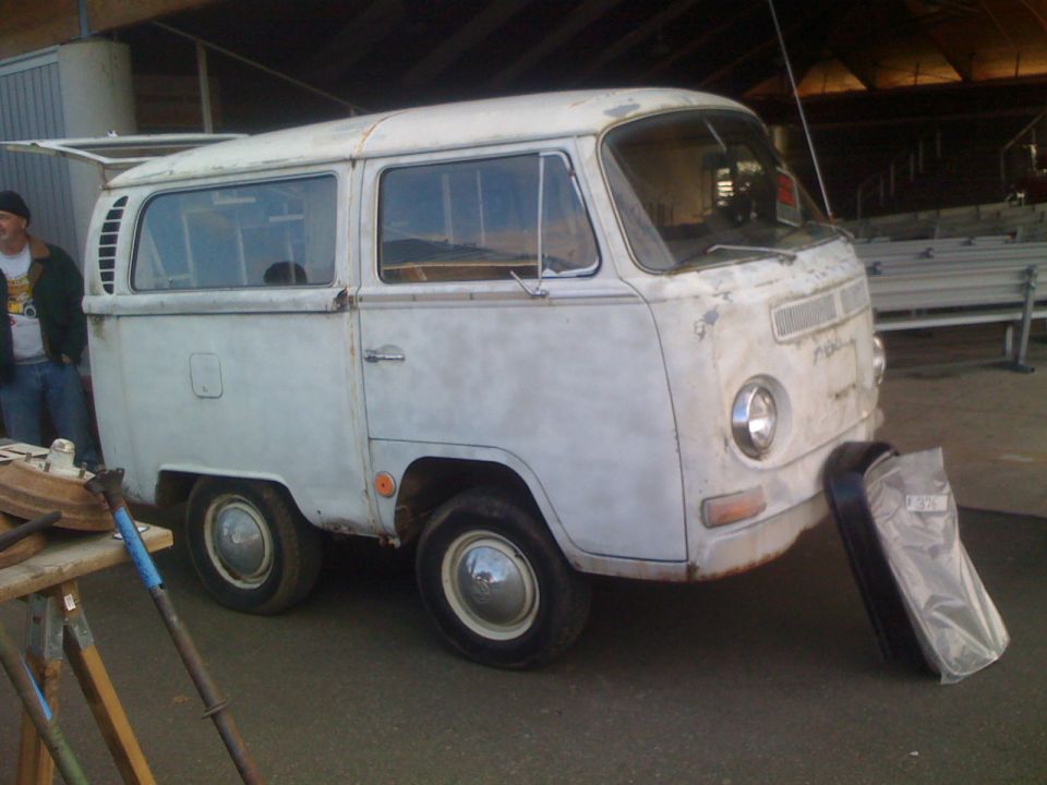 Old white Volkswagen van with louvers on the side, parked outside
