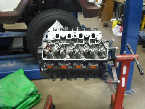 1979 Ford Bronco - A V8 engine block is mounted on a red engine stand in a garage setting.