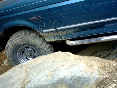 1995 Ford Bronco - A teal Ford Bronco navigates rocky terrain, its side panel displaying the 'Bronco' badge.
