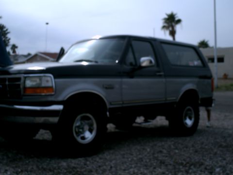 1994 Ford Bronco - This two-tone Ford Bronco SUV is viewed from the front three-quarter angle, showing its side profile and aftermarket wheels.