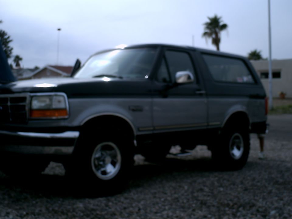 Two-tone gray and black Ford Bronco SUV, side view, with aftermarket wheels and a slightly open driver's door